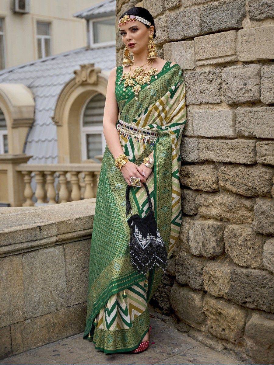 Woman in green and gold ethnic saree with intricate patterns, traditional jewelry, and stone wall backdrop