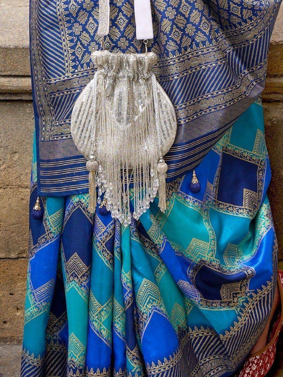 Blue and teal ethnic saree with gold patterns and embellished potli bag, perfect for Indian festive wear