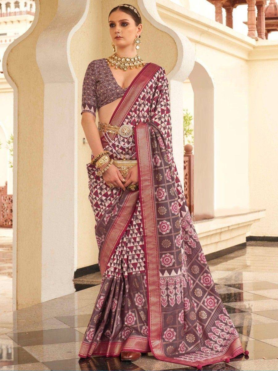 Elegant purple and pink printed saree with geometric patterns, paired with a matching blouse and gold jewelry, perfect for ethnic occasions.