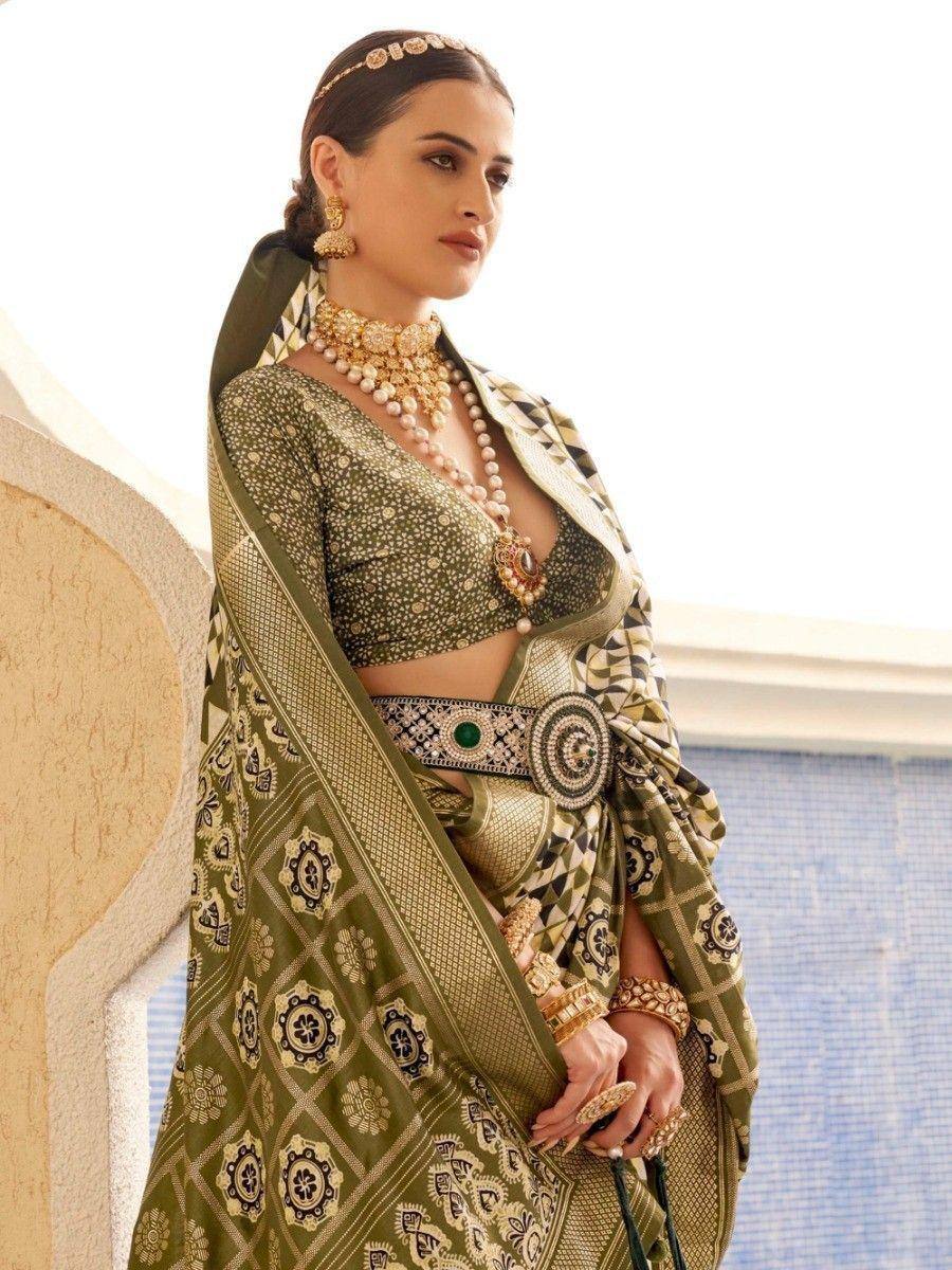 Elegant olive green designer saree with gold embroidery, paired with statement jewelry and a decorative belt.