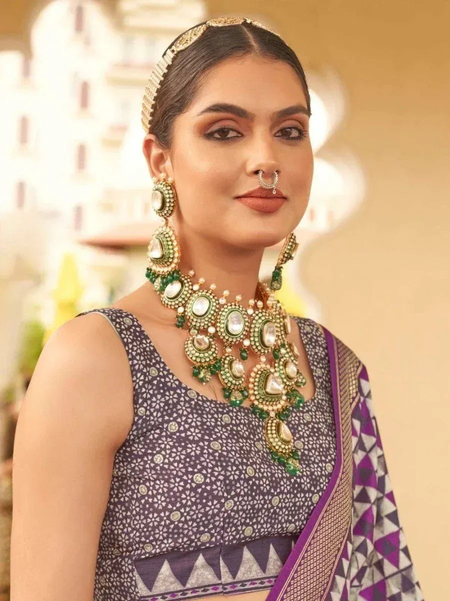 Woman in purple printed saree with green gold jewelry, ethnic Indian wear