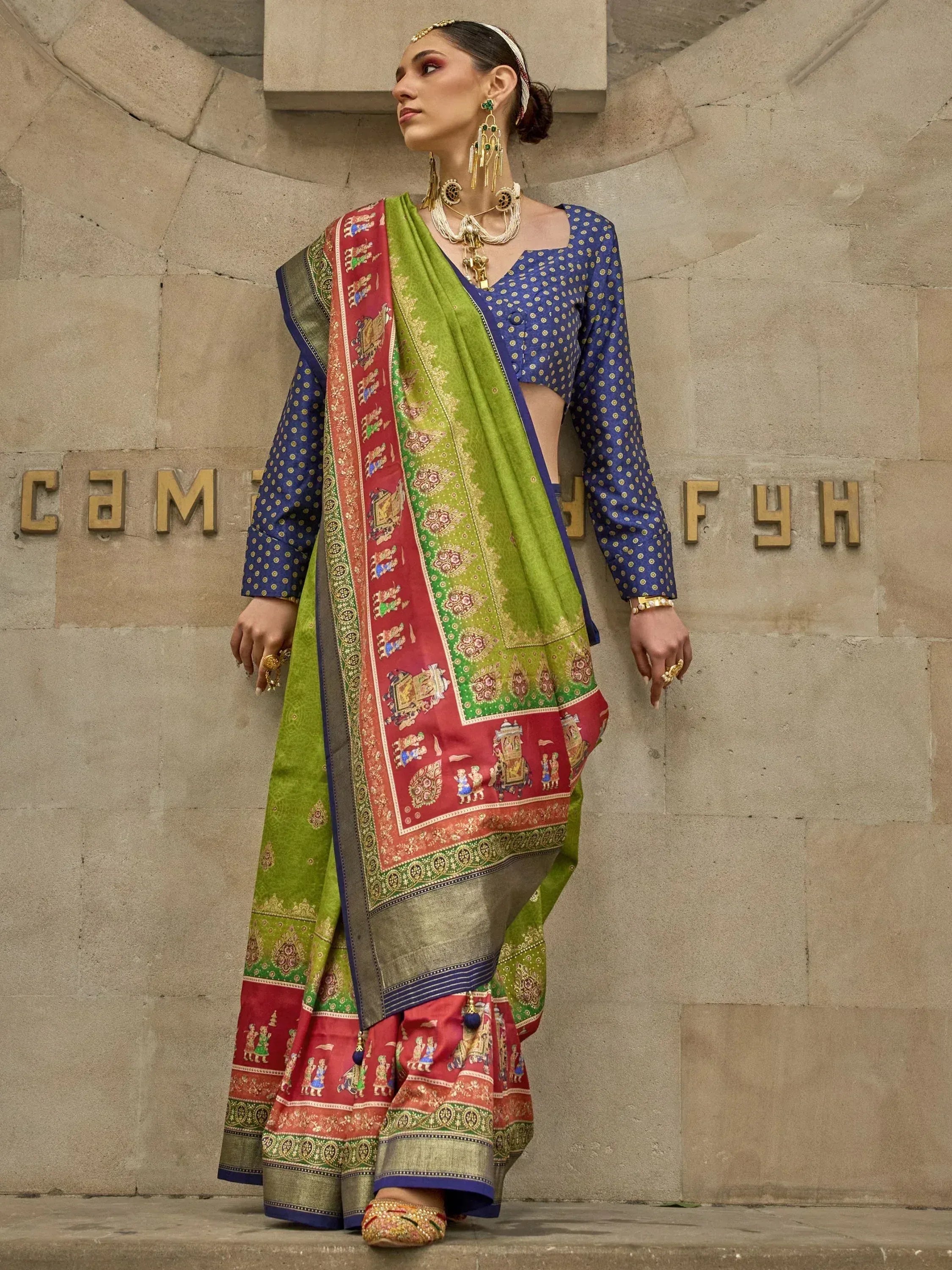 Woman in vibrant green and red printed saree with blue polka dot blouse, ethnic jewelry, traditional Indian wear