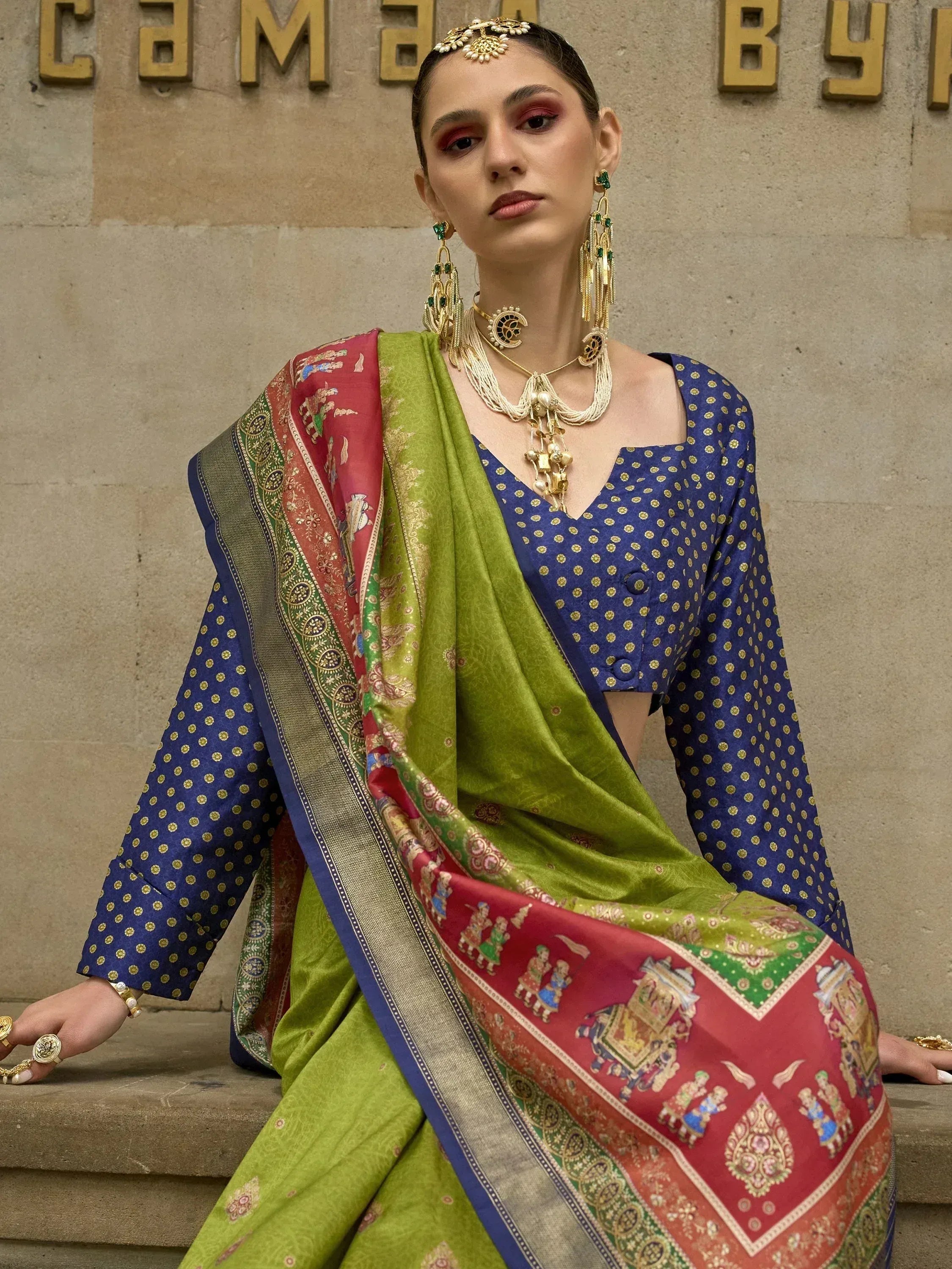 Woman in vibrant green and red printed saree with blue polka dot blouse, styled with traditional gold jewelry for ethnic wear.