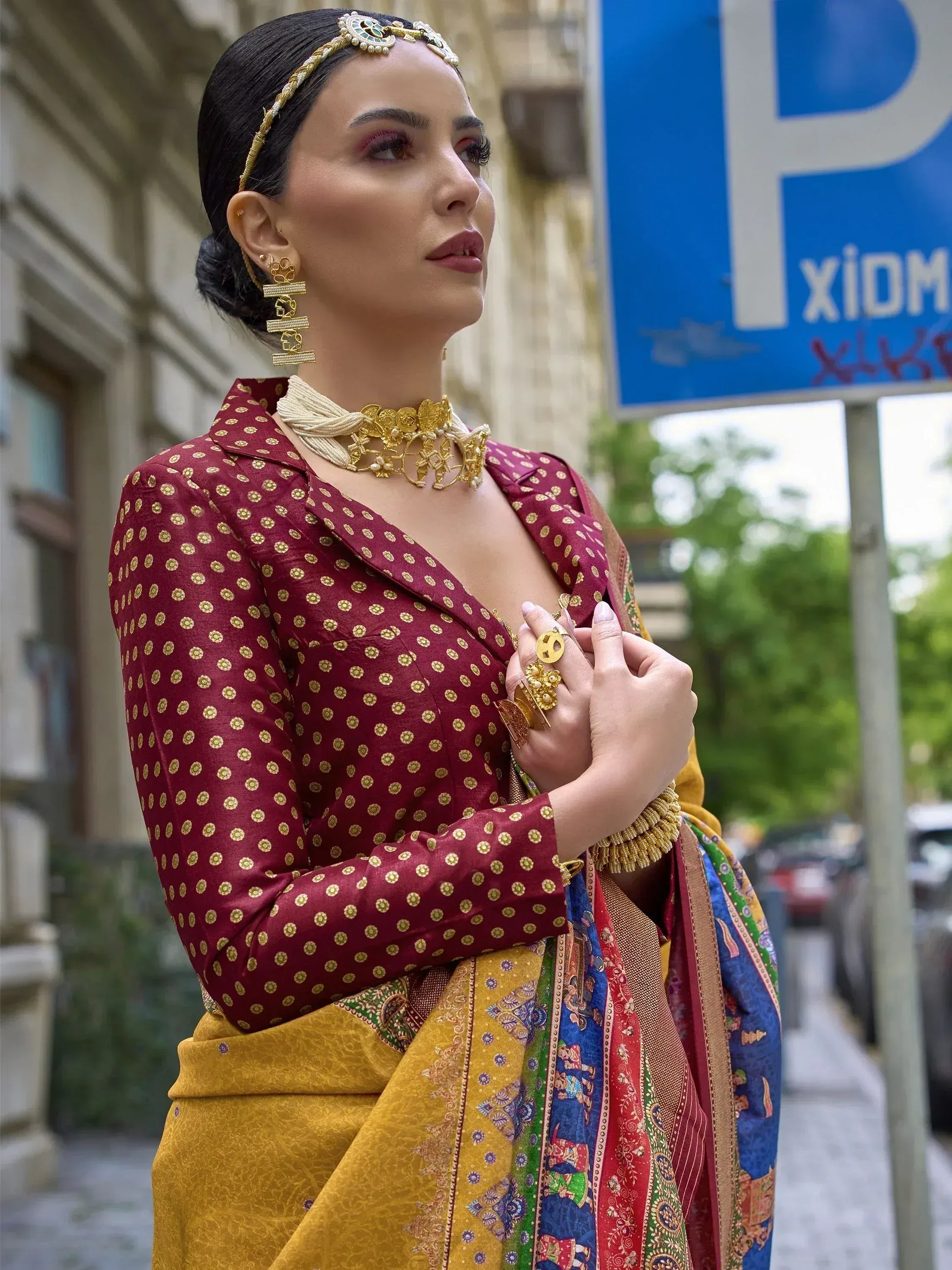 Woman in maroon and gold ethnic blouse with patterned saree, traditional jewelry, street setting