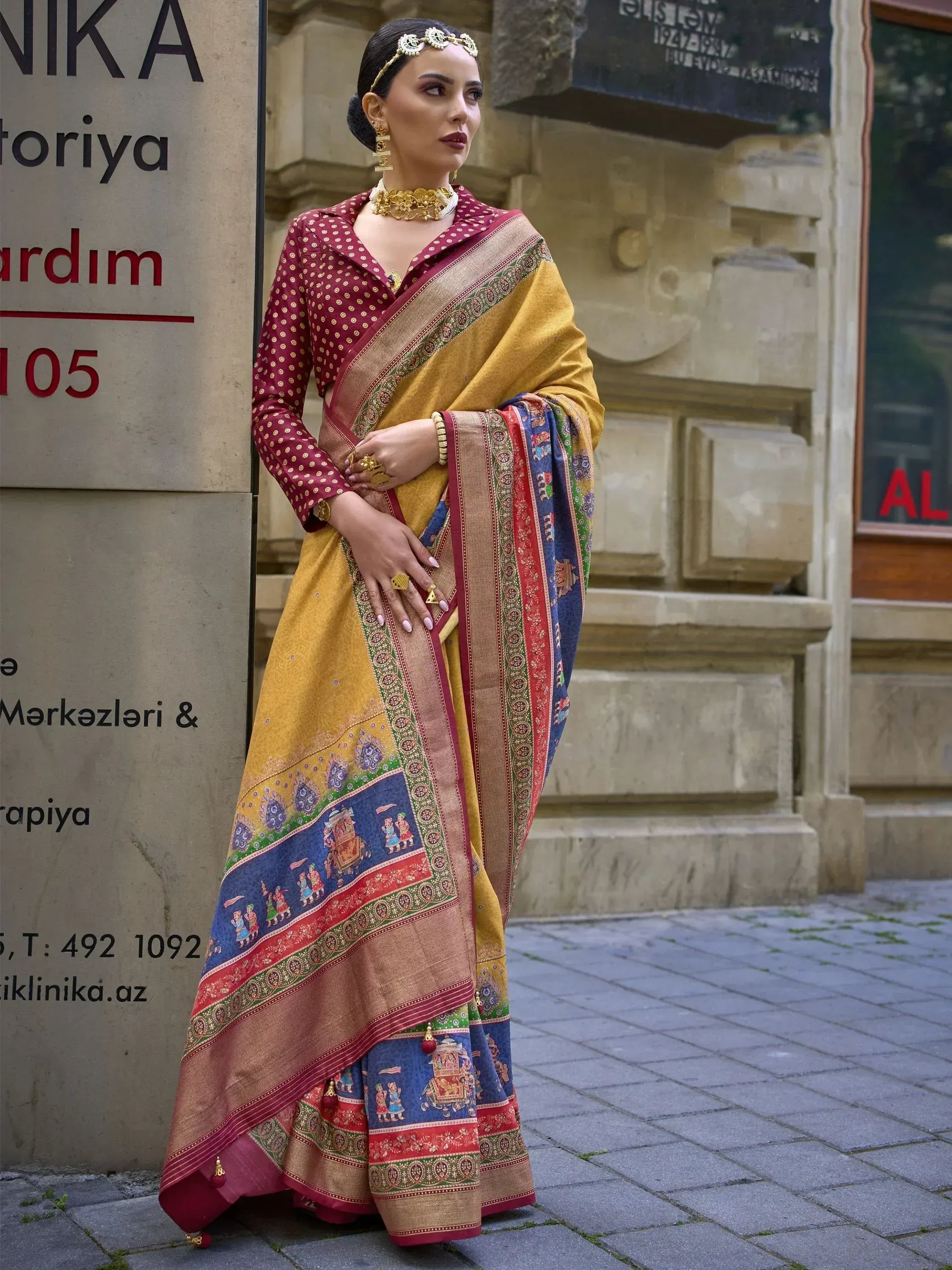 Woman in vibrant yellow and blue printed saree with maroon blouse, traditional Indian ethnic wear