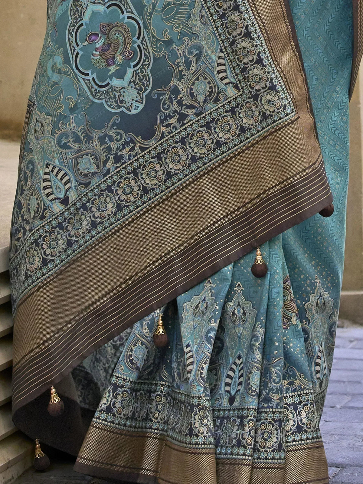 Teal designer saree with peacock motif, gold border, and tassels, perfect for ethnic wear occasions.