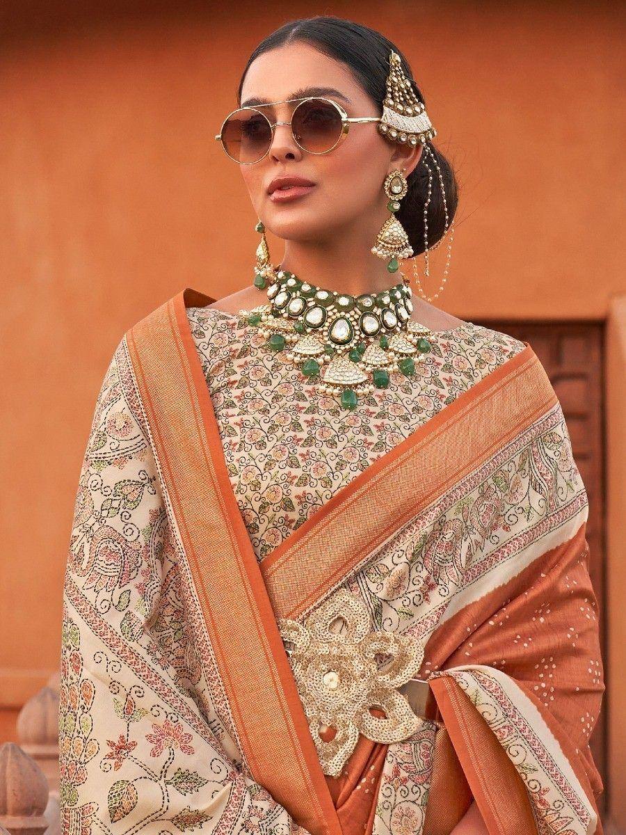 Woman in floral print saree with orange border, green jewelry, and sunglasses for ethnic wear