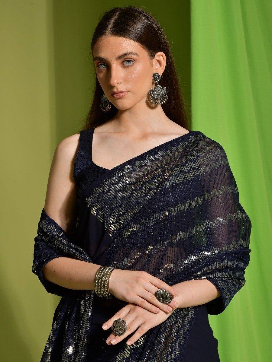 Elegant navy blue sequin saree with gold detailing, styled with statement earrings and rings for festive occasions.