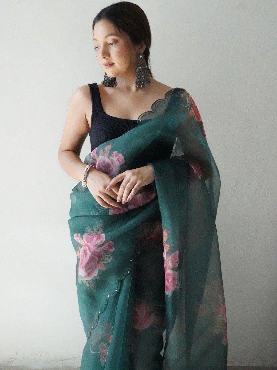 Woman wearing teal floral saree with pink roses, styled with black top and tassel earrings