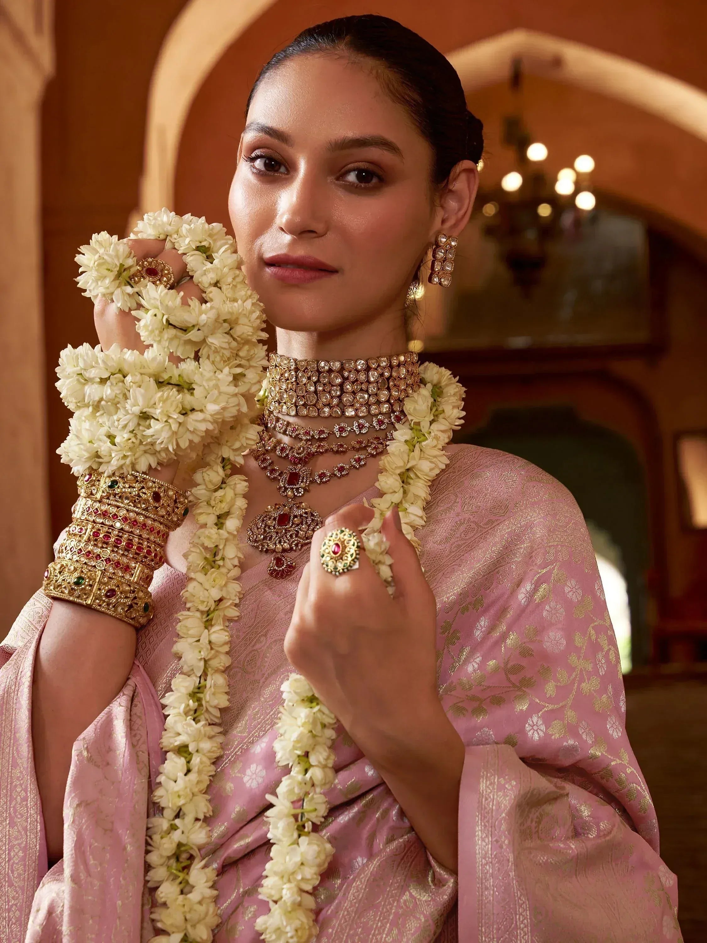 Woman in pink ethnic saree with gold jewelry and floral garland, traditional Indian bridal look