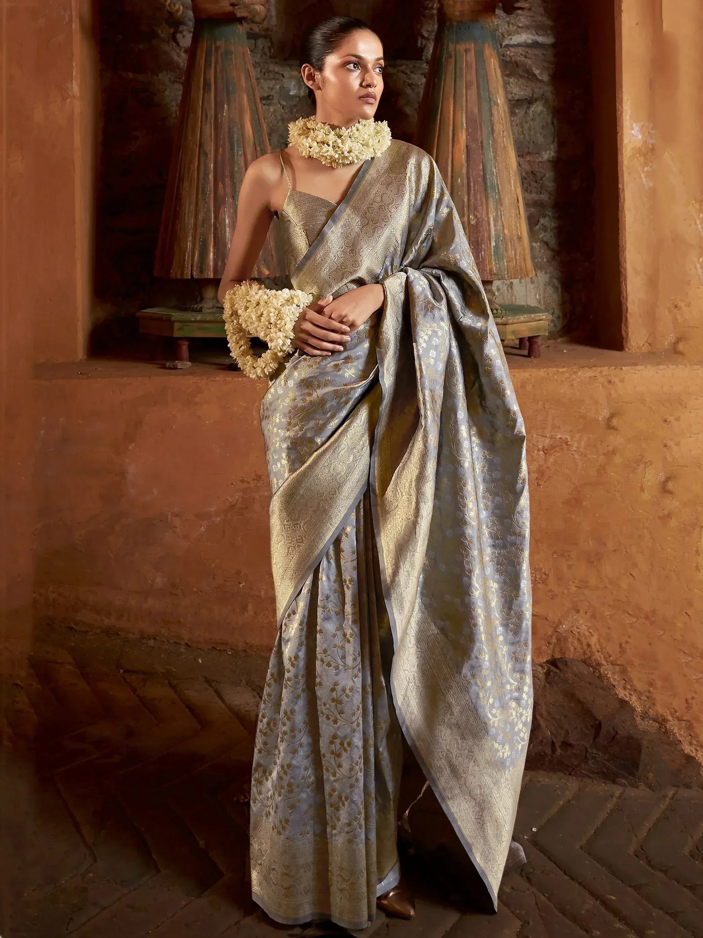 Elegant grey and gold designer saree with floral motifs, paired with floral jewelry, perfect for ethnic occasions.