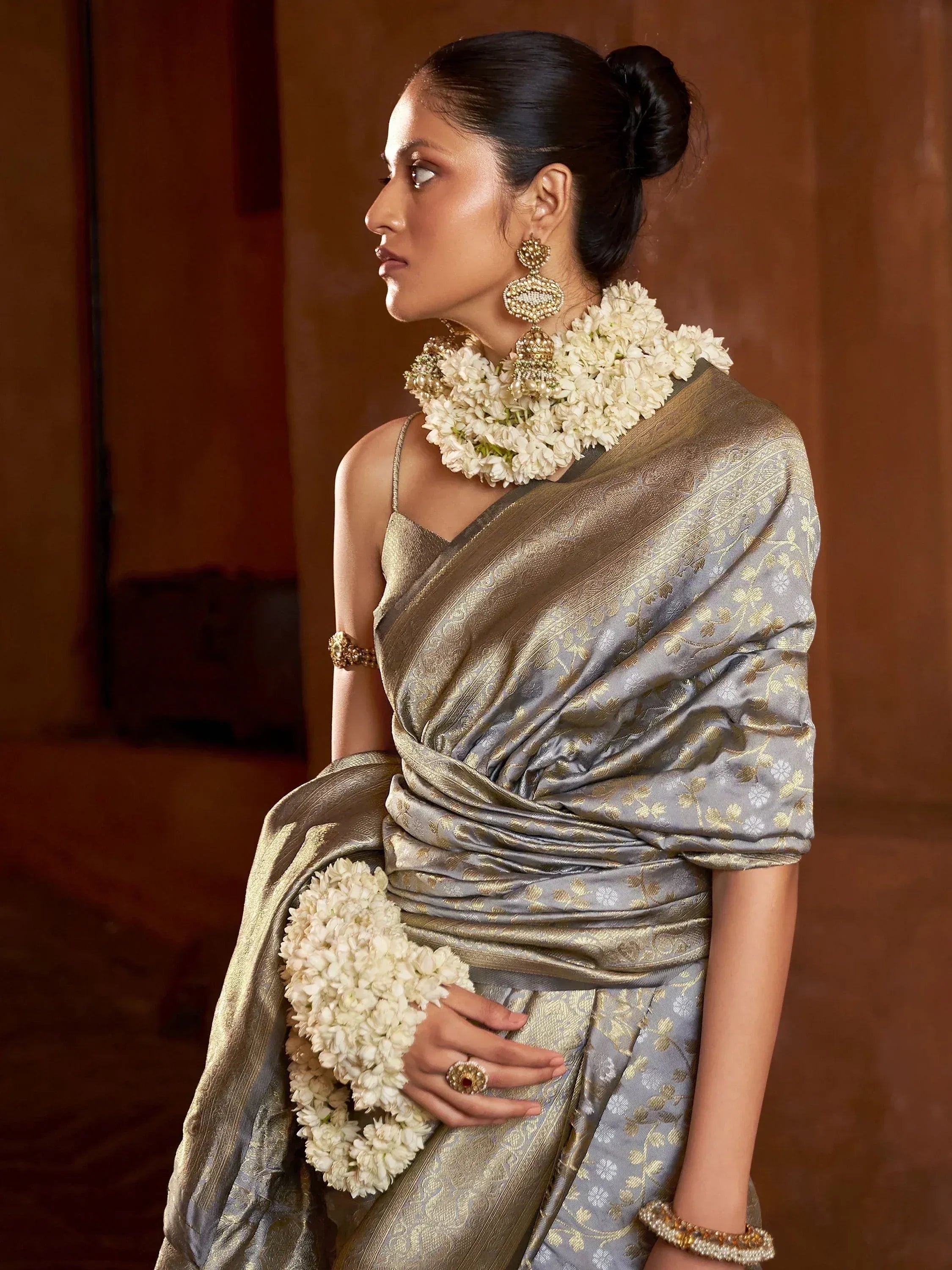 Woman in elegant grey and gold saree with floral garlands and traditional jewelry, showcasing Indian ethnic wear.