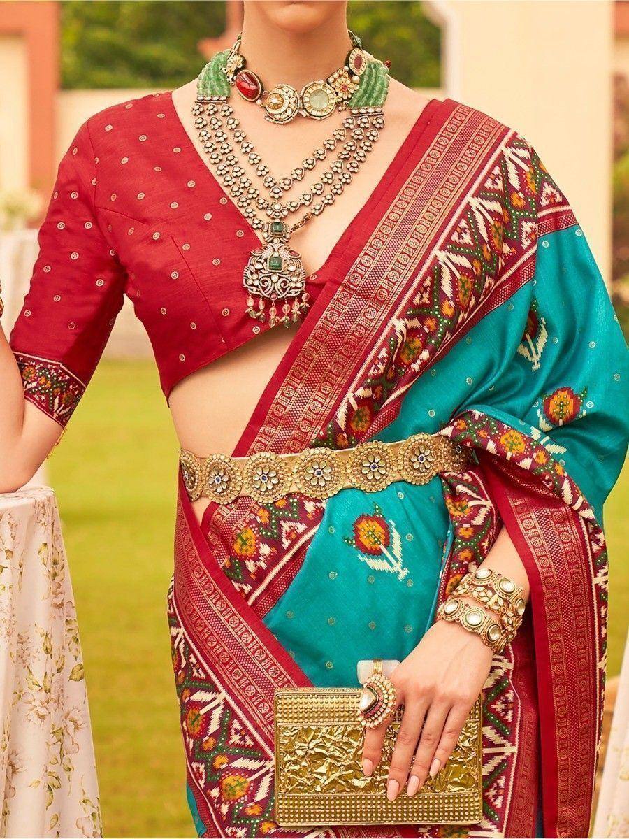 Red and teal ethnic saree with embroidered blouse, statement jewelry, and gold clutch for Indian occasions