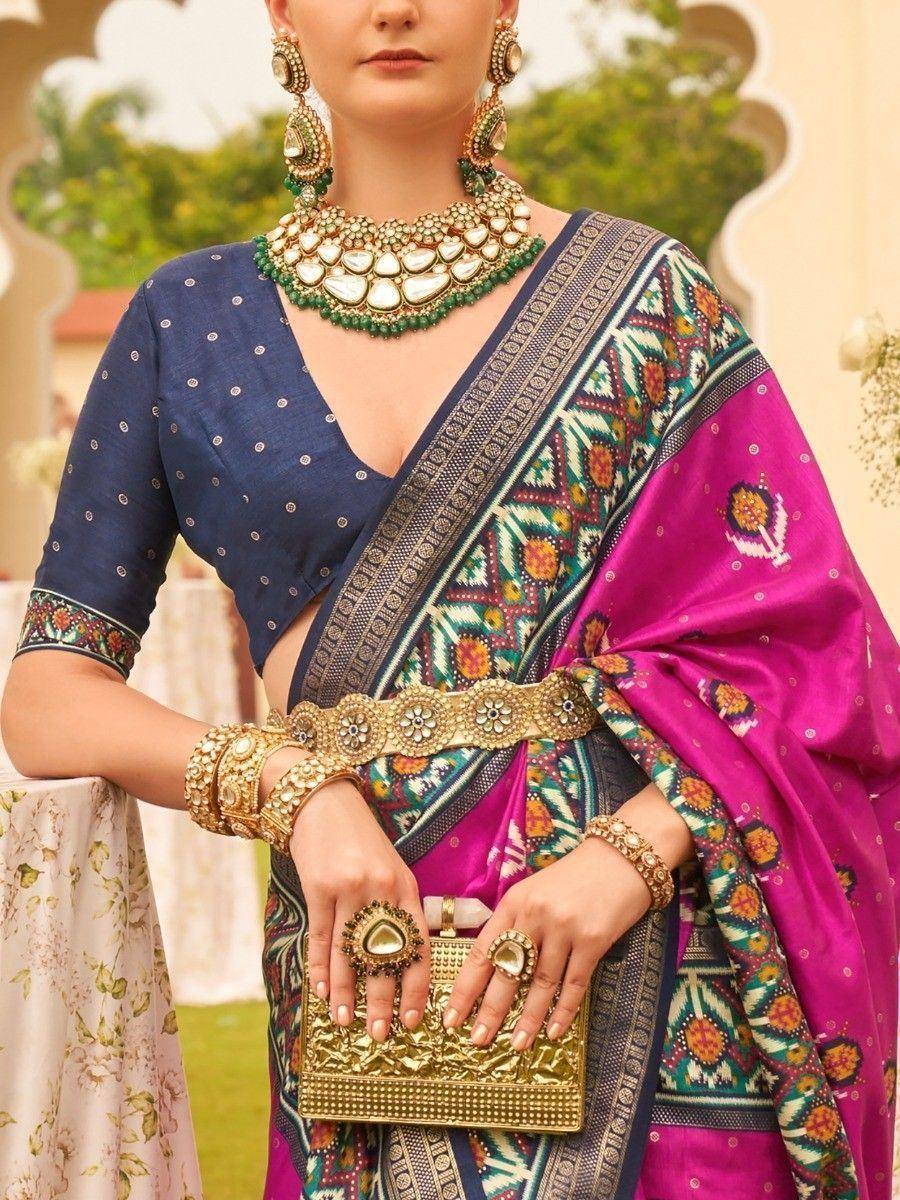 Woman in vibrant pink and blue printed saree with gold jewelry, perfect for Indian ethnic occasions.