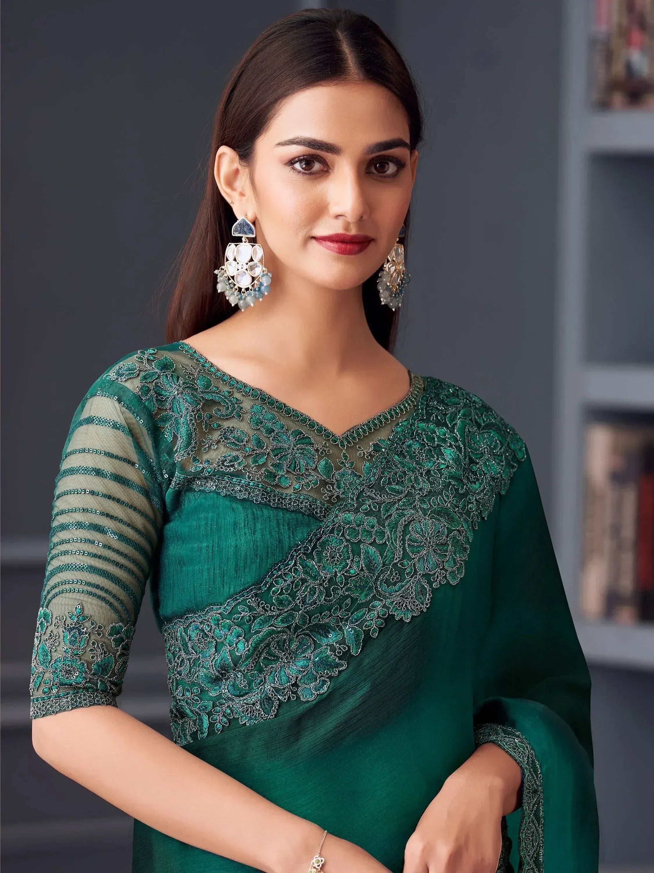 Emerald green embroidered saree with sheer sleeves and floral detailing, paired with statement earrings.