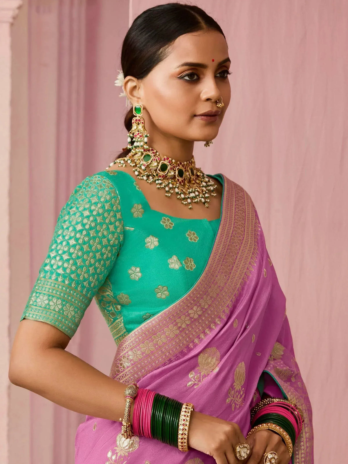 Woman in pink and green designer saree with gold embroidery, traditional Indian jewelry, and floral blouse