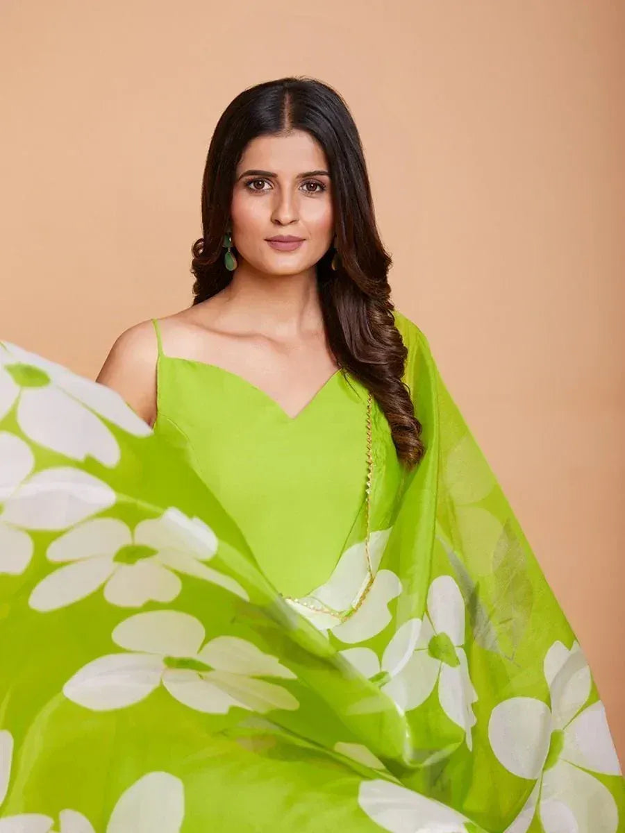 Woman in bright green floral saree with white flower prints, wearing green earrings