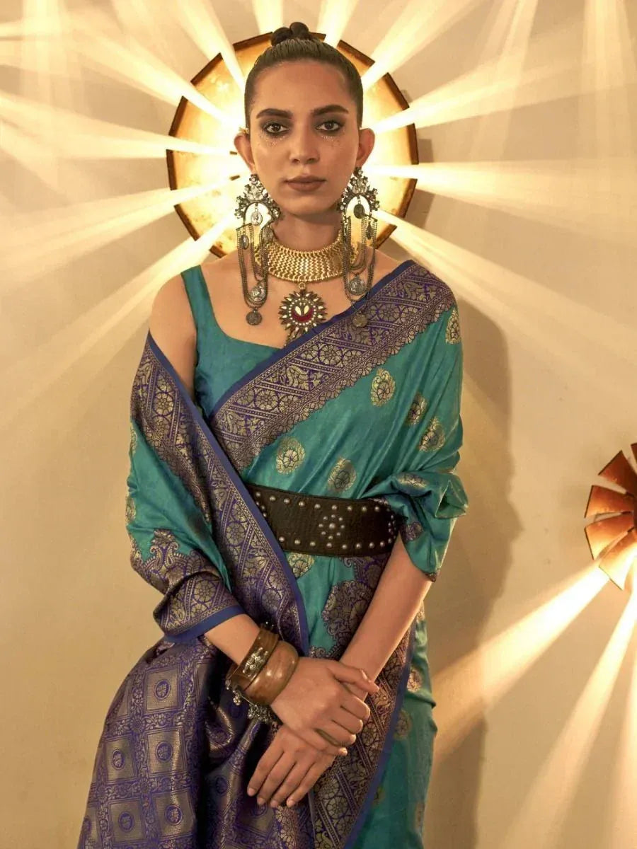 Teal and purple designer saree with gold embroidery, paired with statement jewelry and a modern belt.
