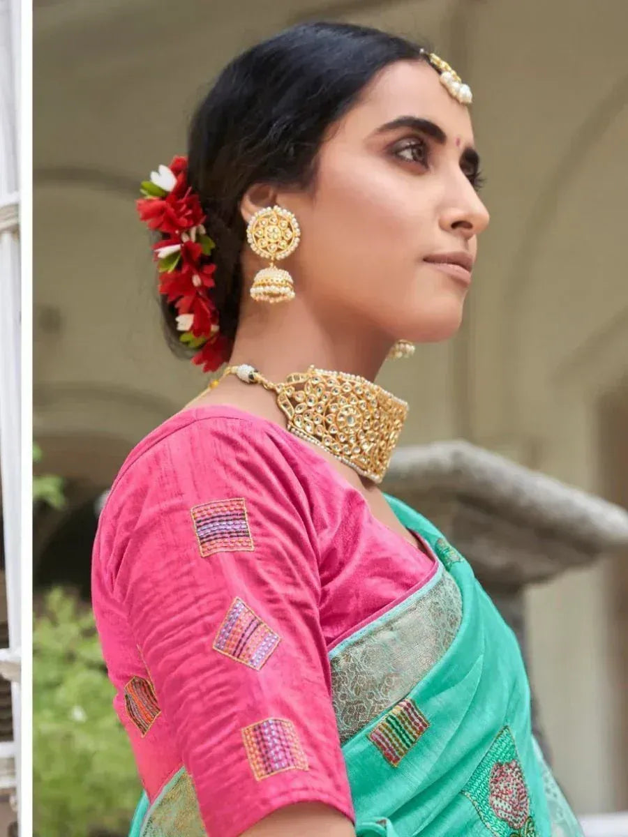 Woman in pink blouse and green saree with floral hair accessory and gold jewelry