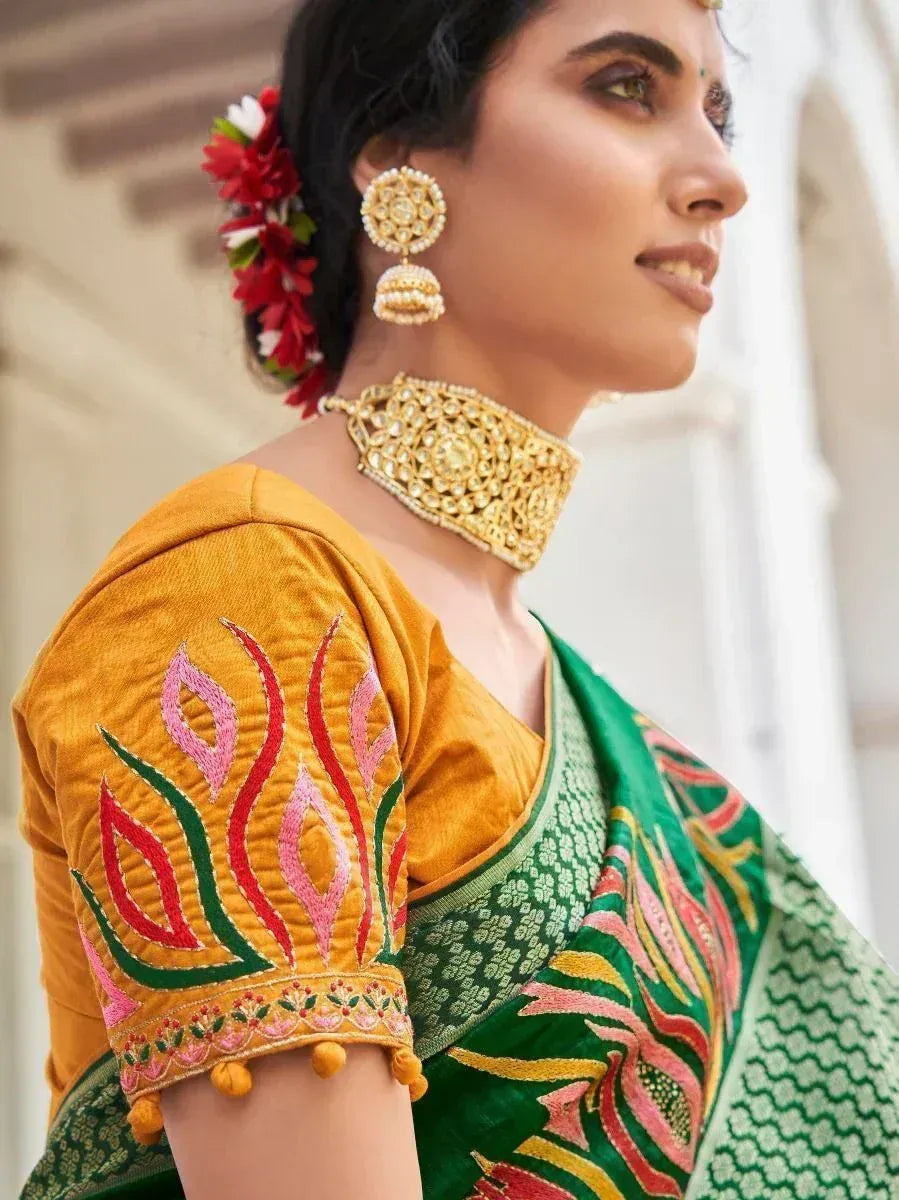 Woman in vibrant green and yellow embroidered saree with floral motifs, gold jewelry, and floral hair accessory