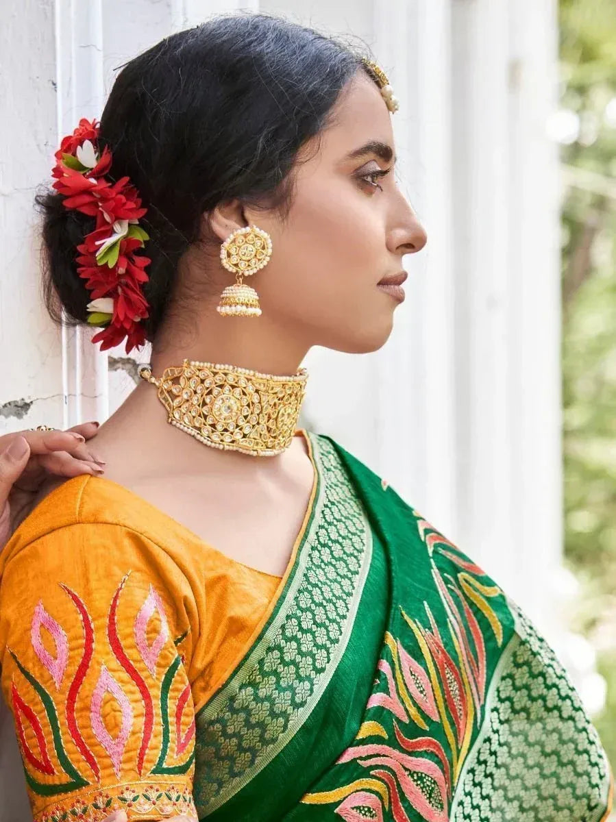Woman in vibrant green and orange embroidered saree with gold jewelry and floral hair accessory