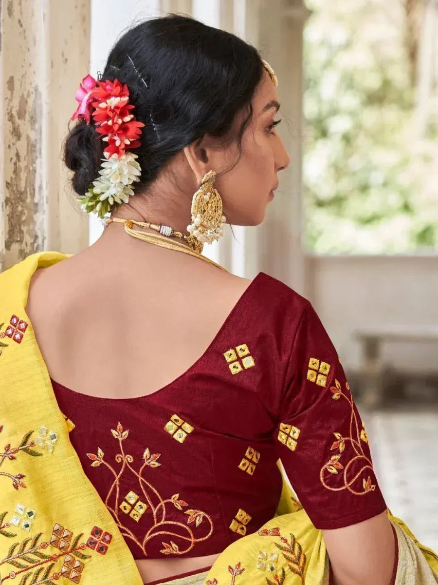 Maroon embroidered blouse with yellow saree, floral hair accessories, and gold jewelry for ethnic wear