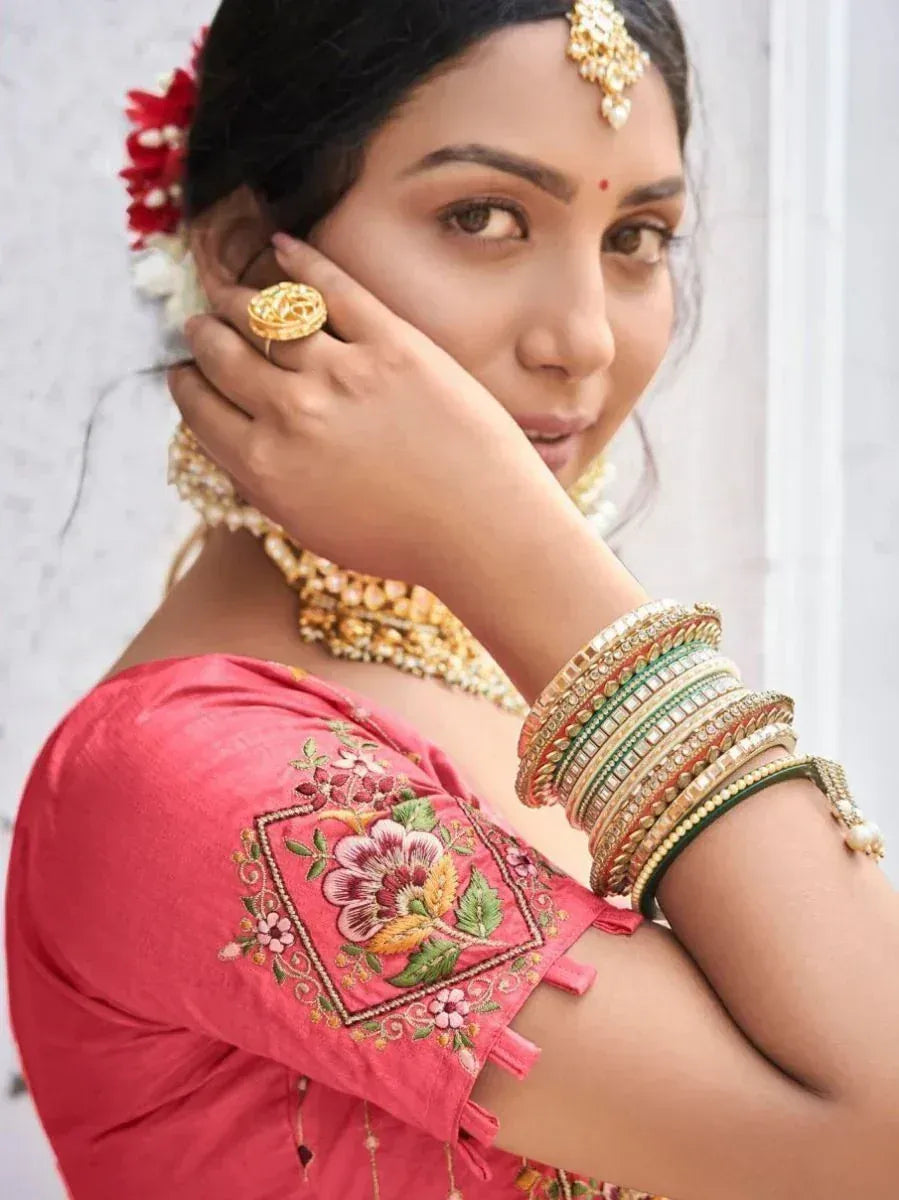 Woman in pink embroidered blouse with gold jewelry and floral hair accessory, showcasing Indian ethnic wear.