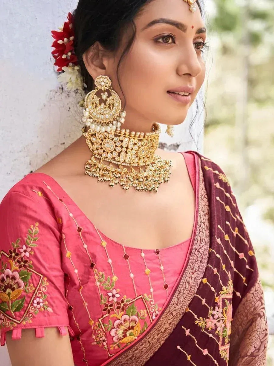 Woman in pink embroidered blouse and maroon saree with gold jewelry, floral hair accessory