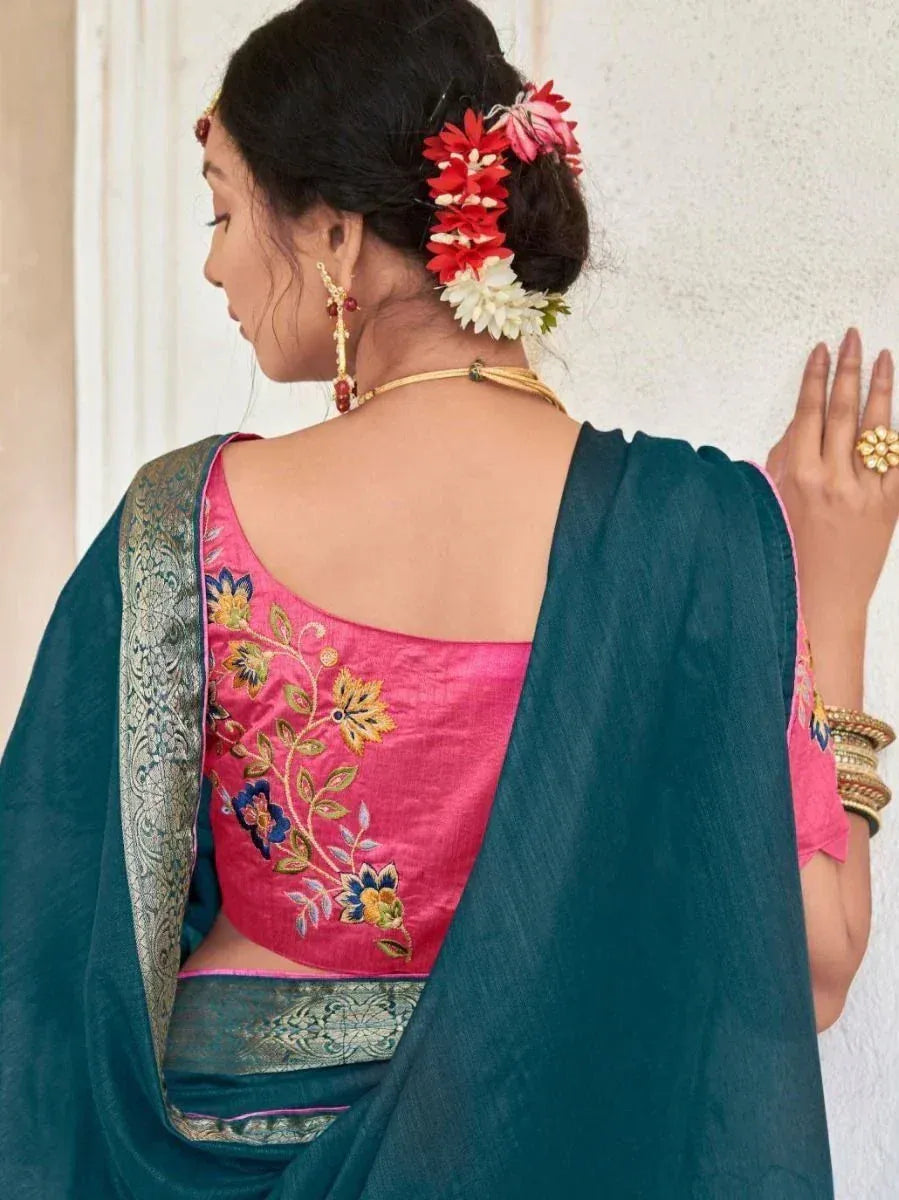 Woman in teal saree with pink embroidered blouse, floral hair accessories, and gold jewelry
