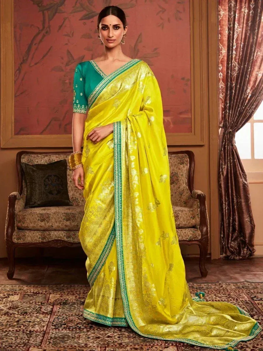 Vibrant yellow saree with green border and floral motifs, paired with teal blouse, perfect for Indian ethnic occasions.