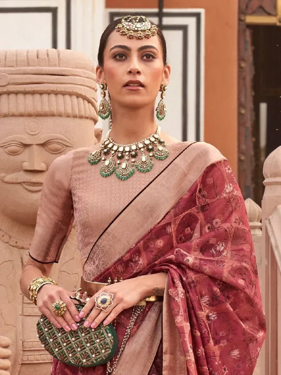 Elegant woman in maroon floral saree with gold blouse, emerald jewelry, and traditional Indian headpiece