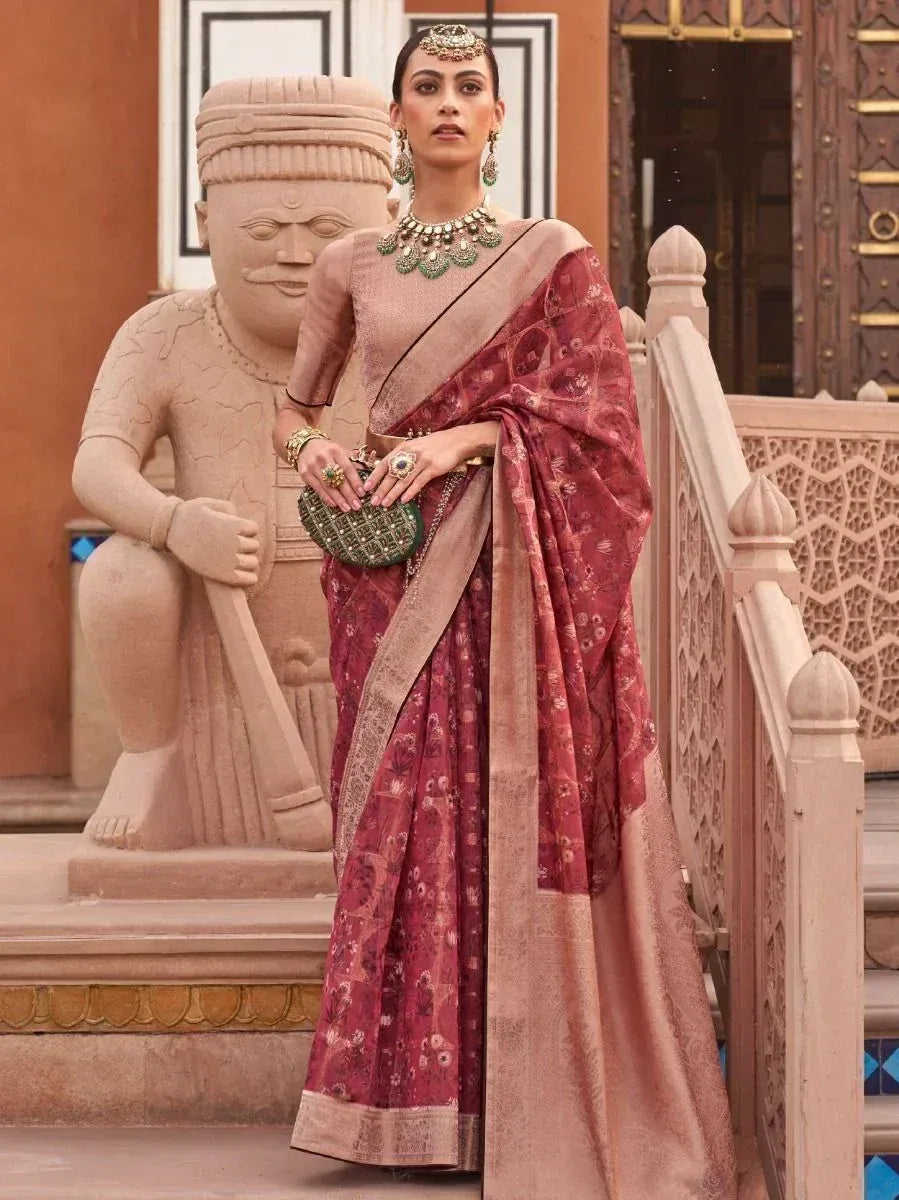 Woman in maroon floral saree with gold border, traditional Indian ethnic wear, styled with green jewelry and clutch