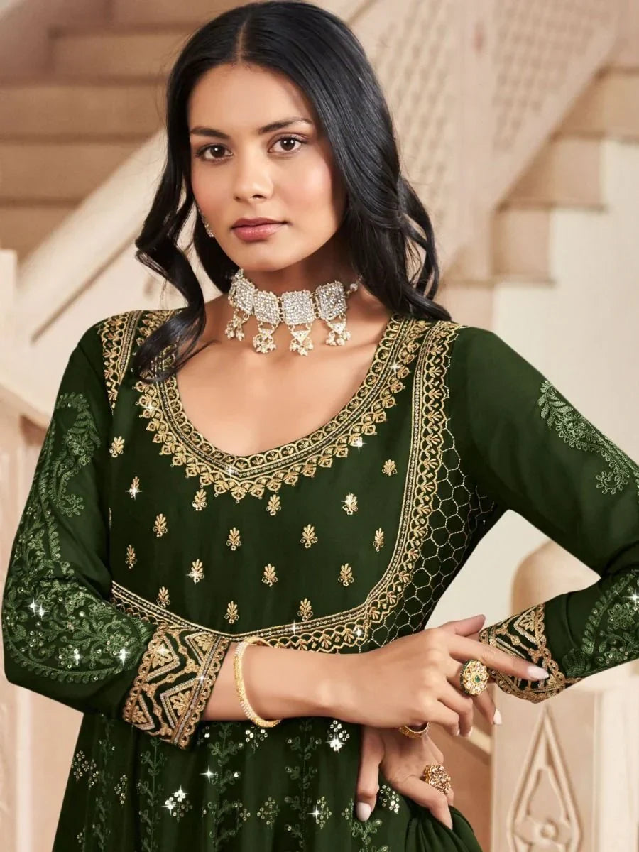 Woman wearing dark green embroidered ethnic gown with gold jewelry, posing indoors