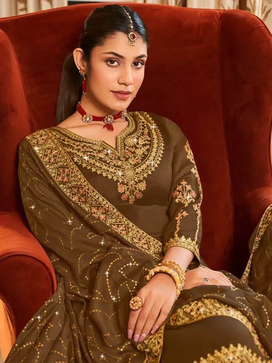 Woman in elegant brown embroidered salwar kameez with gold detailing, seated on red velvet chair