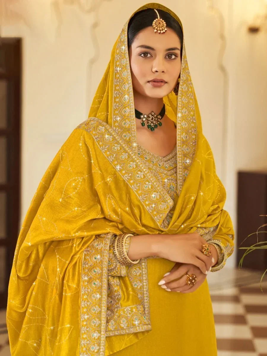 Woman in yellow embroidered salwar kameez with dupatta, traditional jewelry, elegant setting