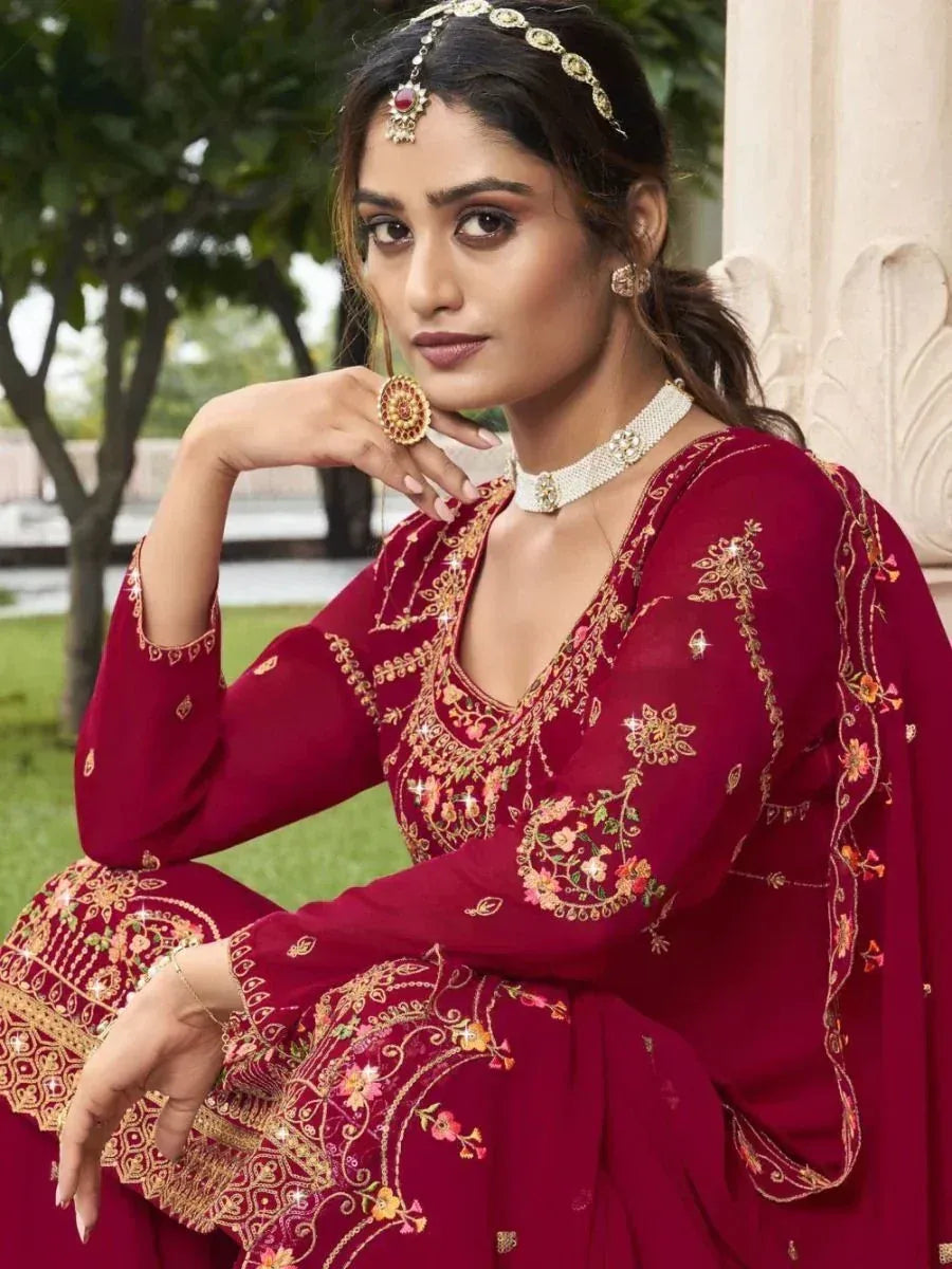 Woman in maroon embroidered Indian ethnic suit with gold jewelry, seated outdoors
