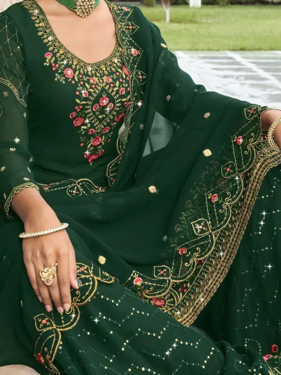 Green ethnic gown with gold and red floral embroidery, worn with traditional jewelry.