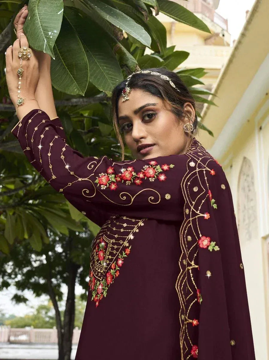Woman in maroon embroidered salwar kameez with floral patterns, standing outdoors