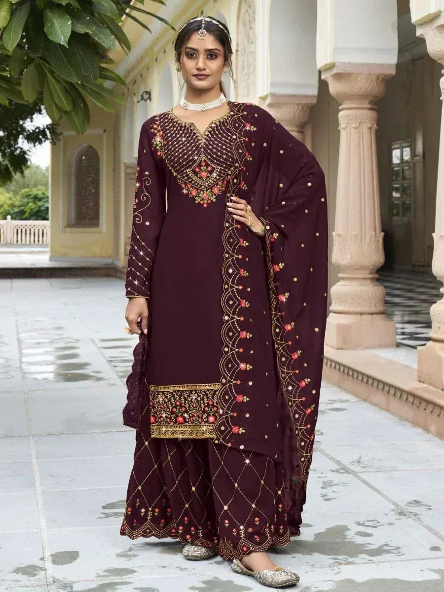 Woman wearing maroon embroidered salwar kameez with dupatta, standing outdoors by pillars