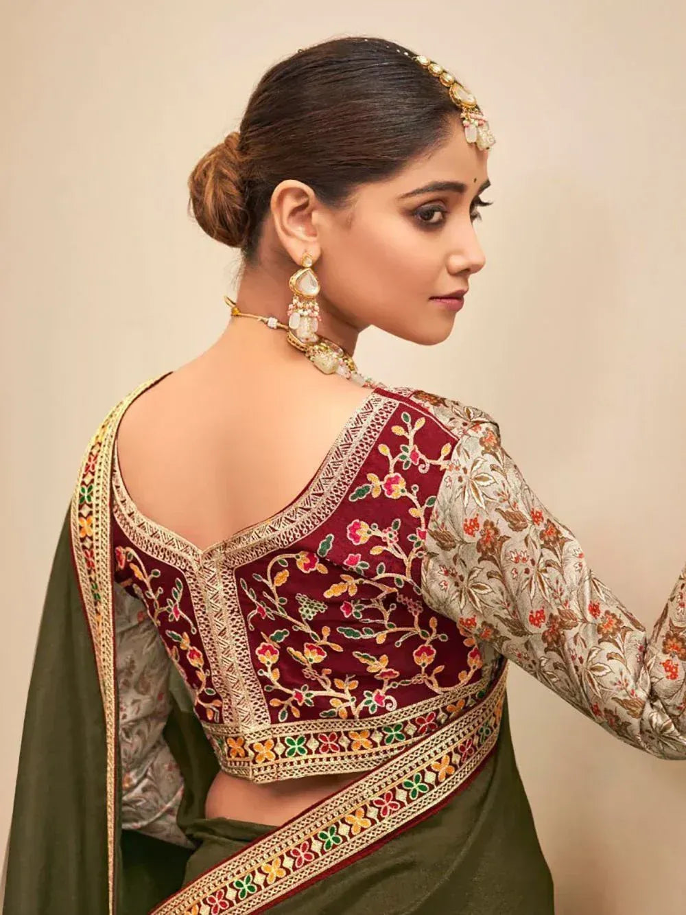Maroon embroidered blouse with floral design, paired with olive green saree and traditional jewelry