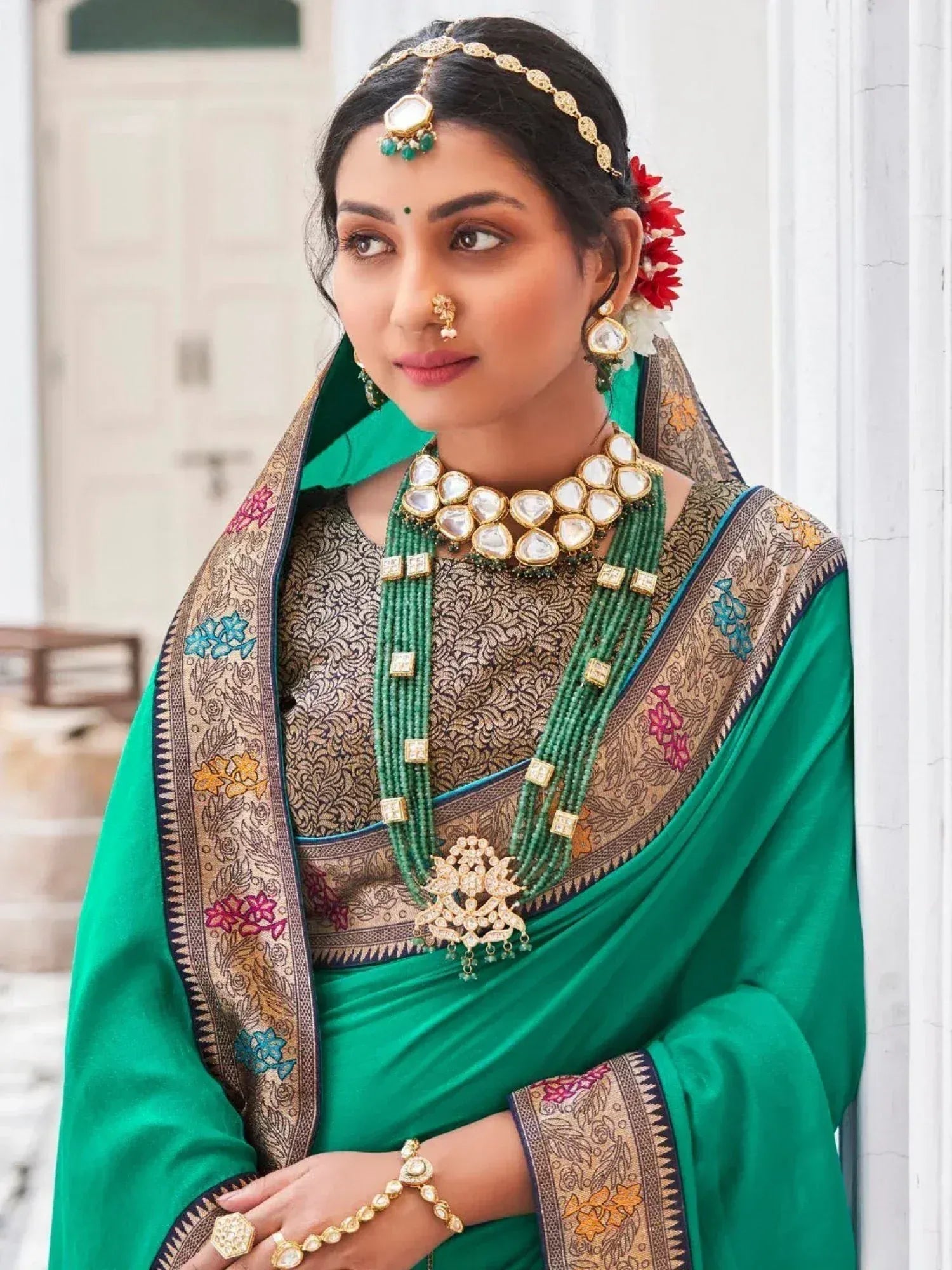 Woman in green embroidered saree with gold jewelry and floral hair accessories