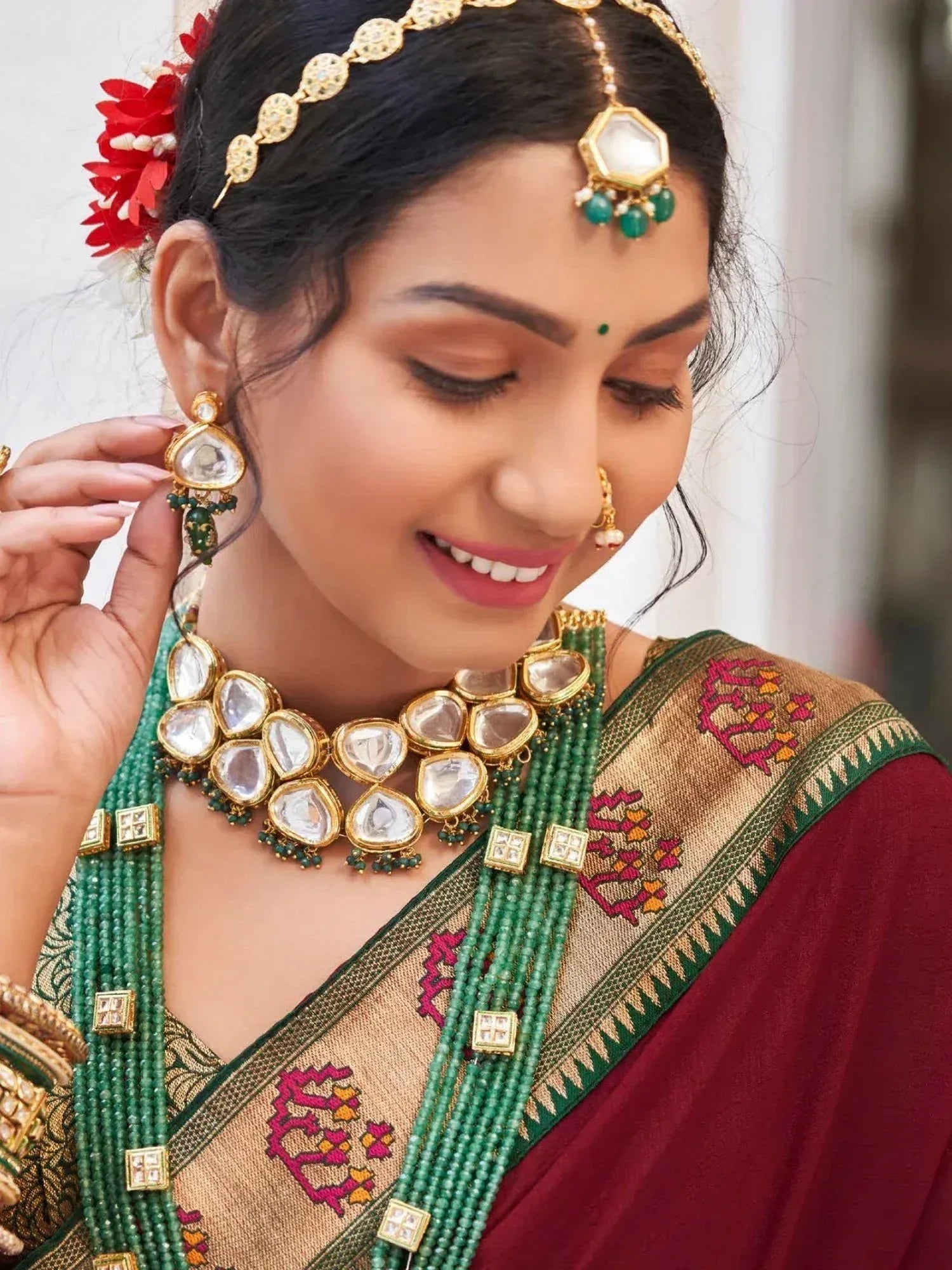 Woman in traditional Indian saree with gold and green jewelry, floral hair accessory, and bindi