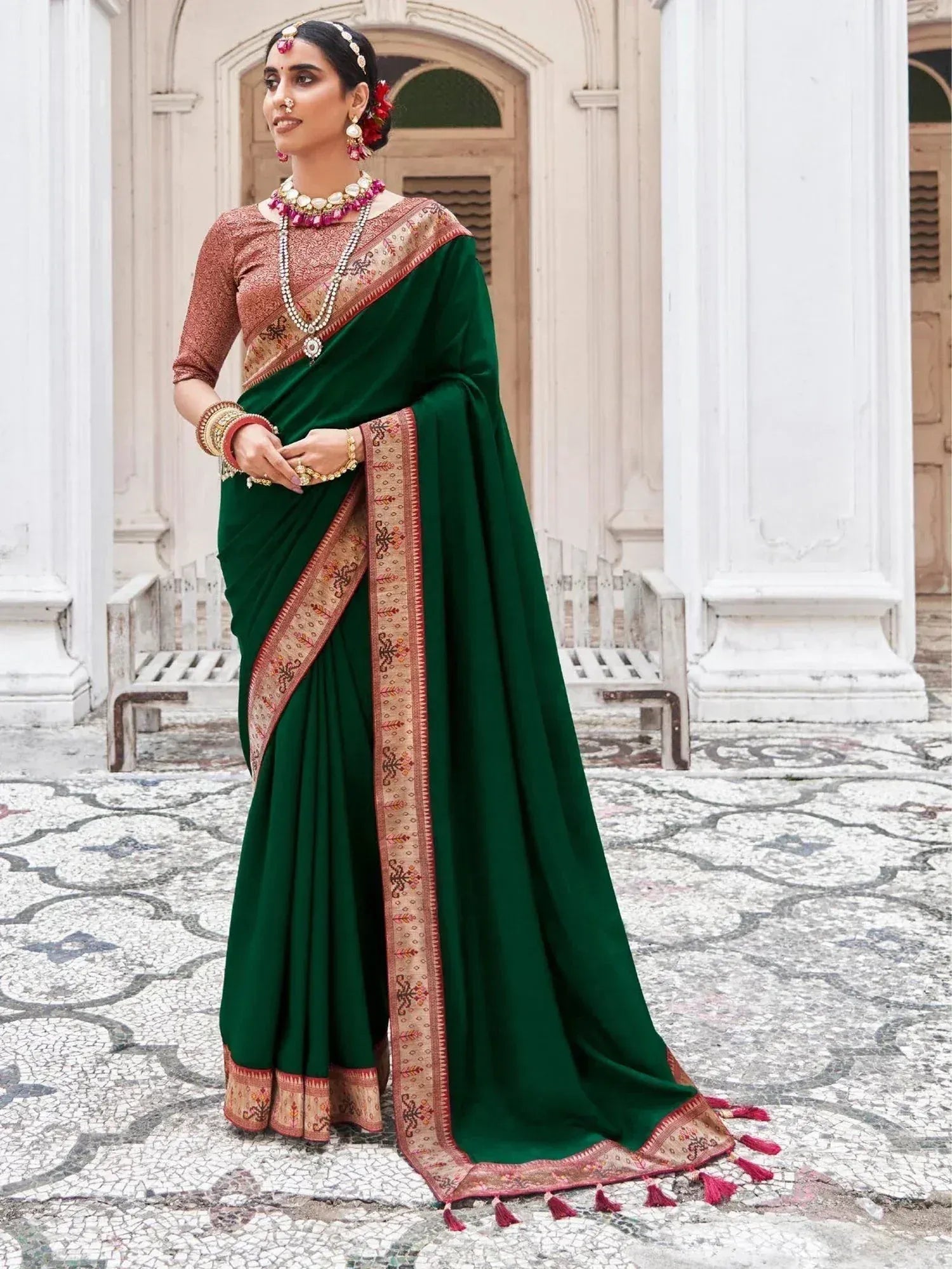 Emerald green designer saree with gold border and tassels, paired with matching blouse and traditional jewelry
