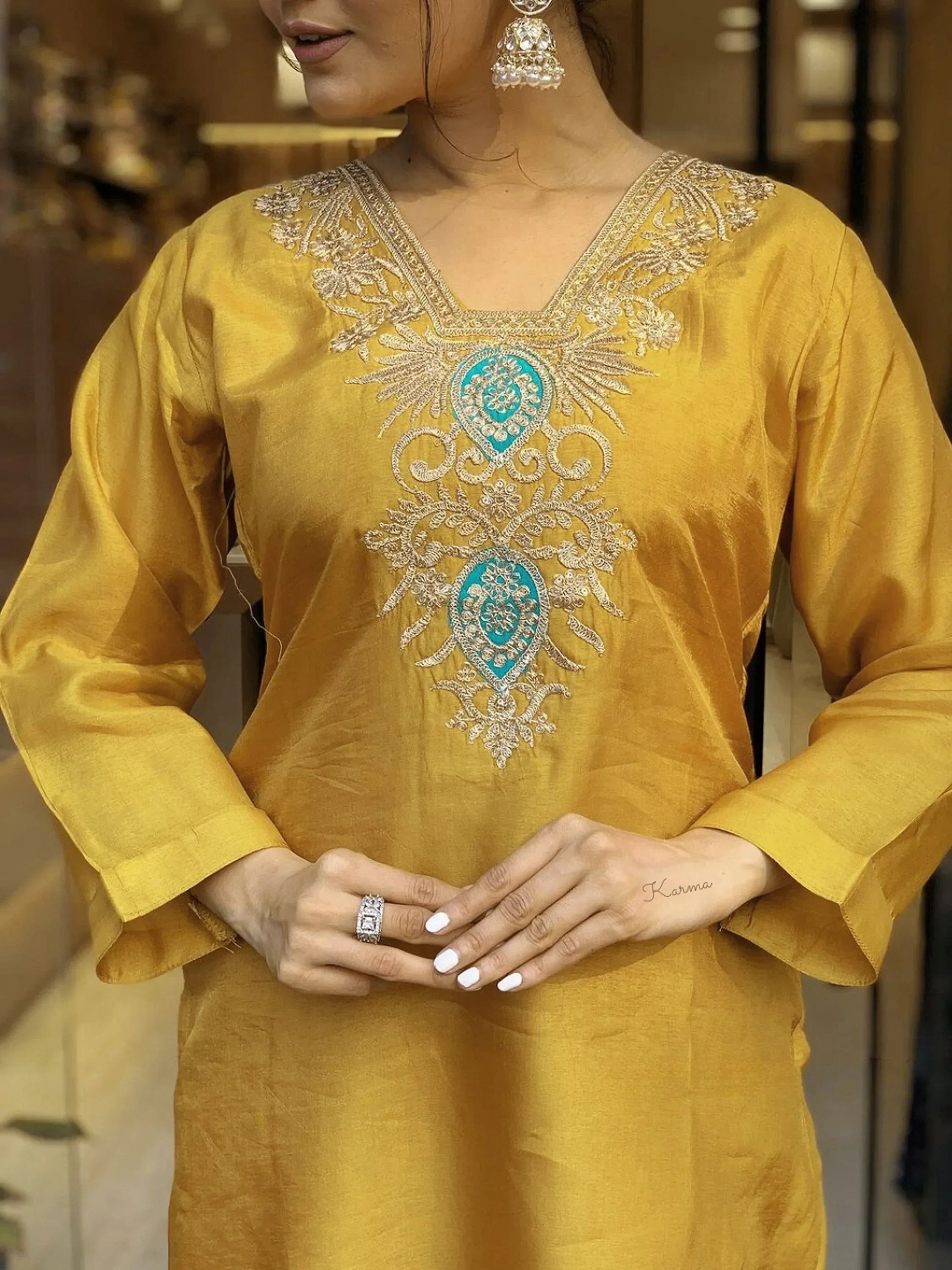 Woman in mustard yellow kurta with intricate embroidery, wearing jhumka earrings