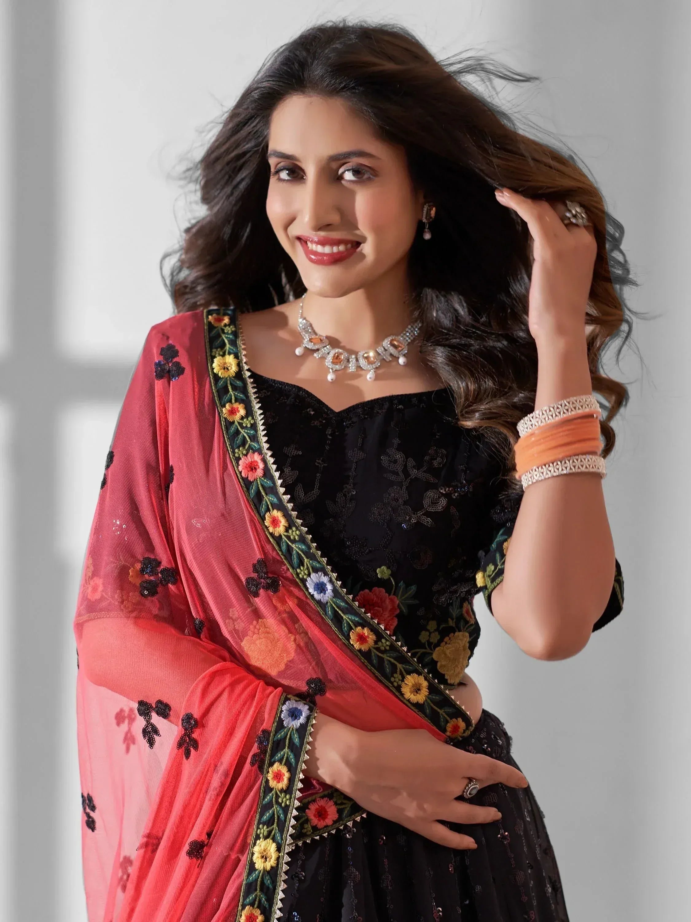 Elegant black embroidered lehenga with vibrant red dupatta, floral detailing, and traditional jewelry