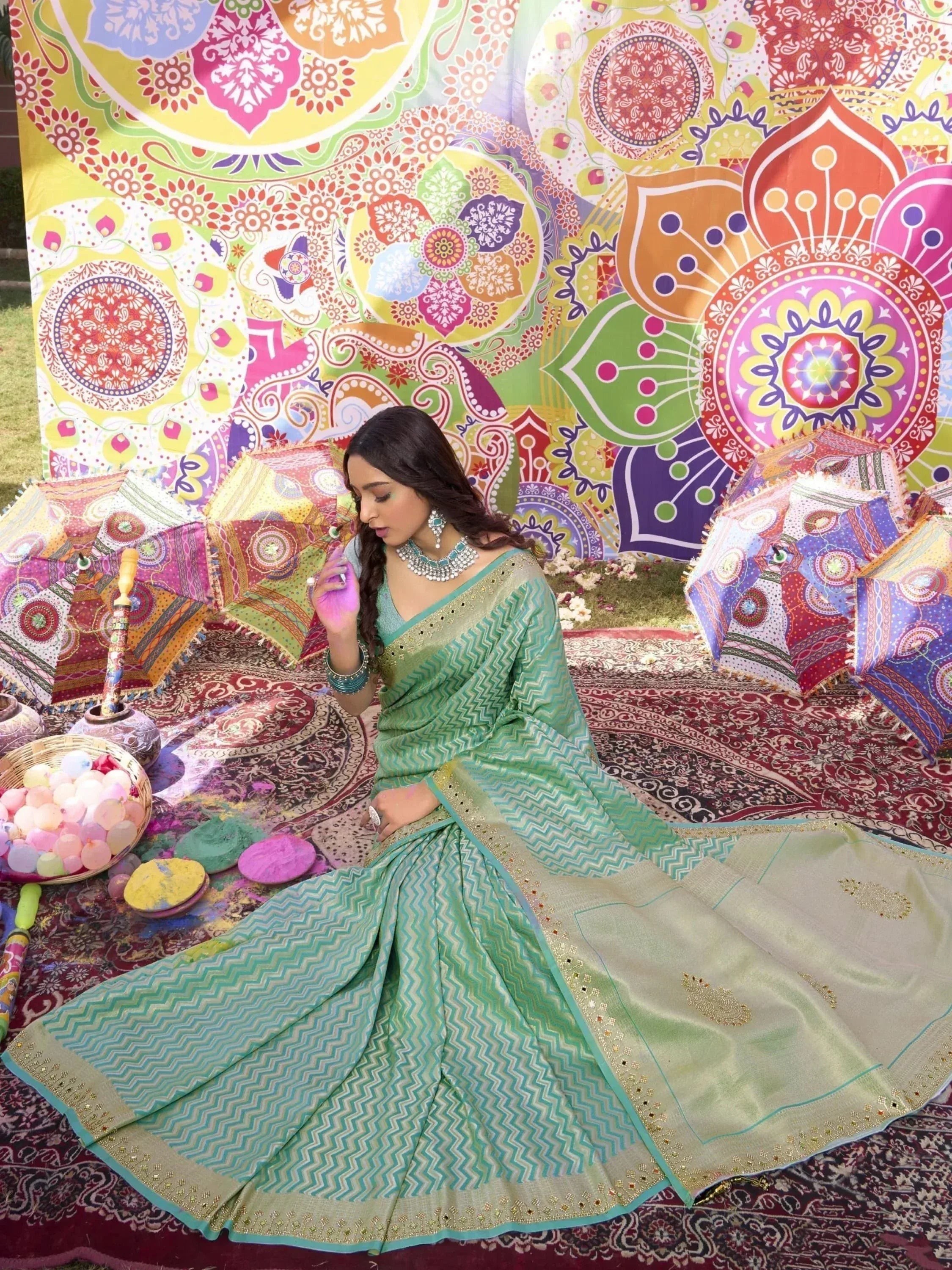 Woman in green zigzag saree with gold border, Holi colors, and patterned backdrop for festive ethnic wear