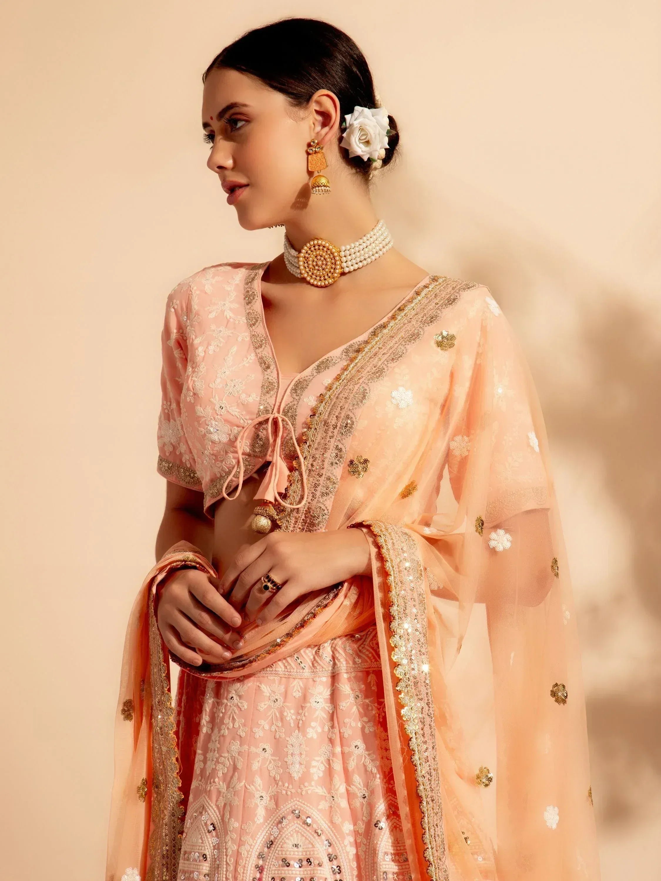 Elegant peach lehenga choli with gold embroidery, floral dupatta, and traditional jewelry for Indian ethnic wear.