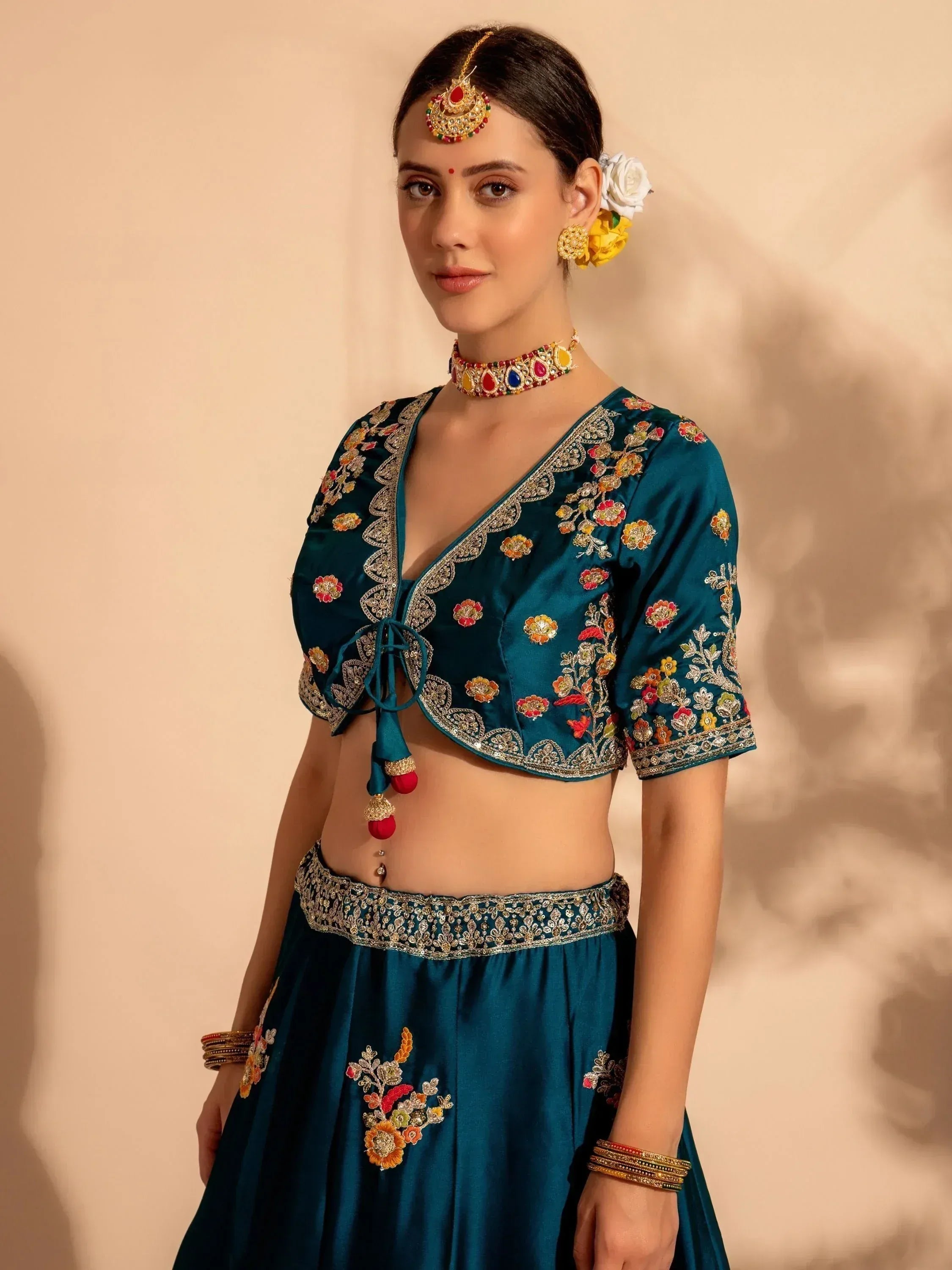 Teal embroidered lehenga choli with floral motifs, traditional jewelry, and temple-style accessories for Indian ethnic wear.