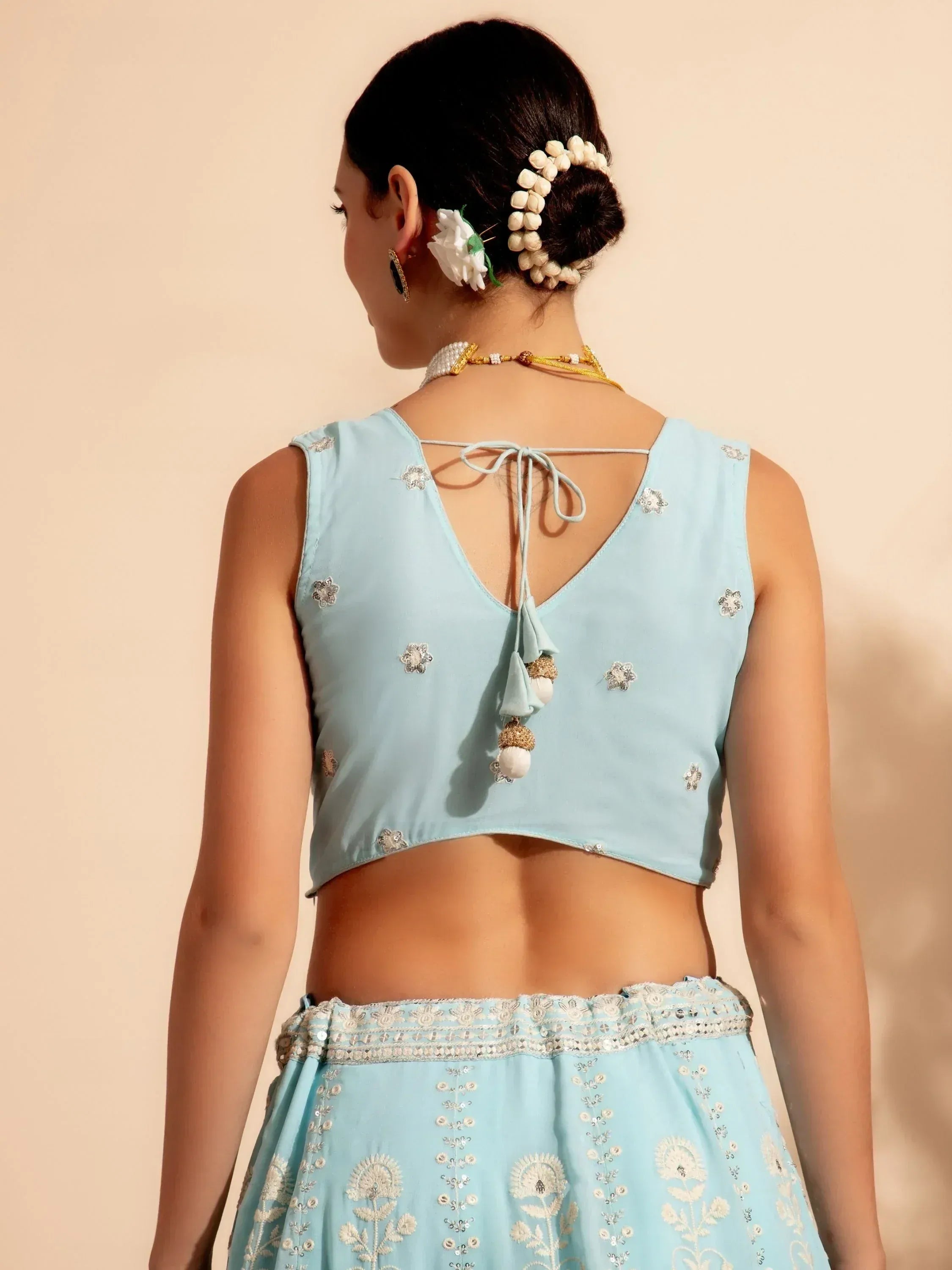 Light blue embroidered lehenga choli with back tie detail, floral hair accessories, and traditional jewelry