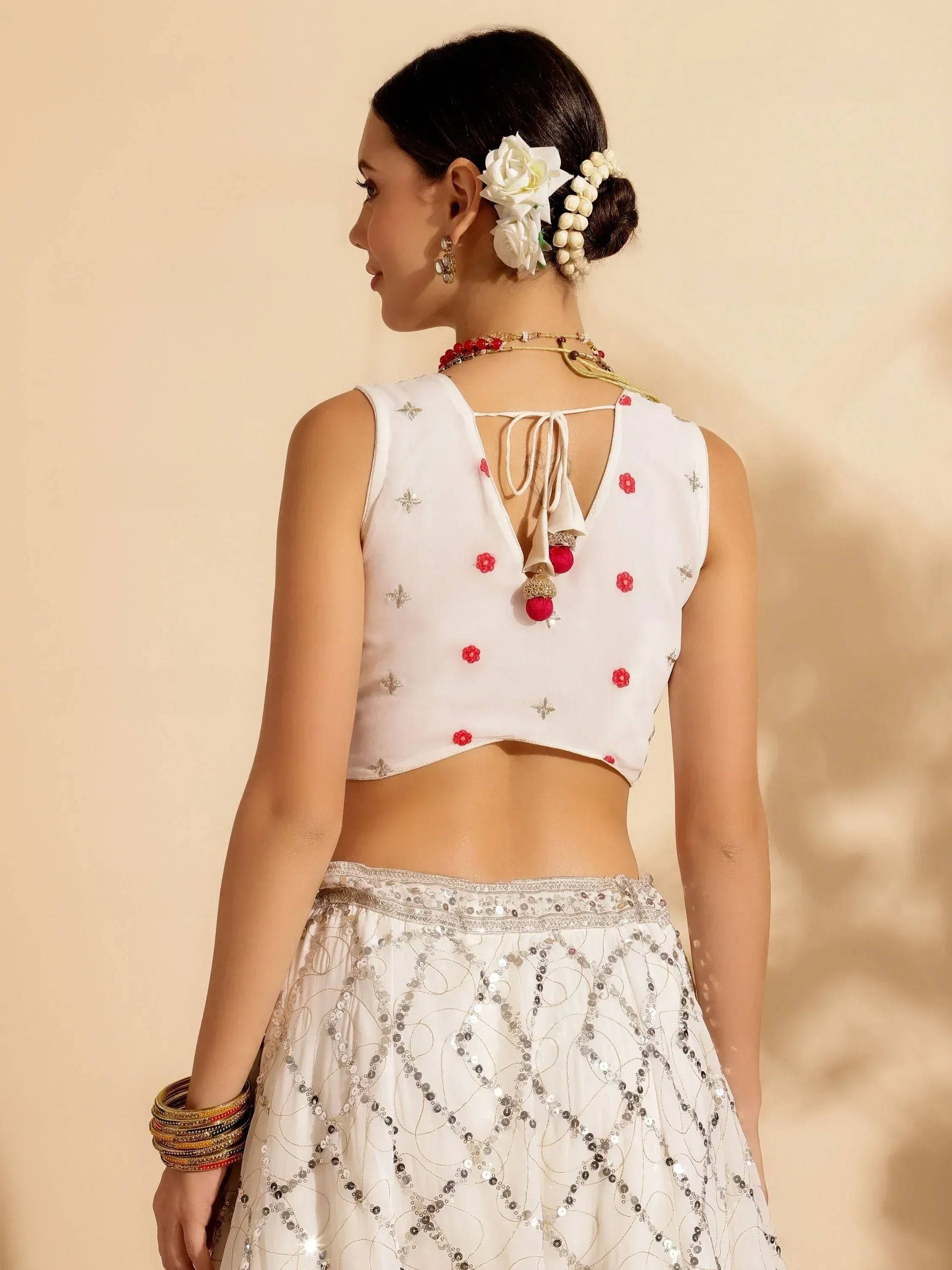 White ethnic lehenga choli with red floral embroidery, back tie blouse, and sequin skirt, styled with flowers and bangles